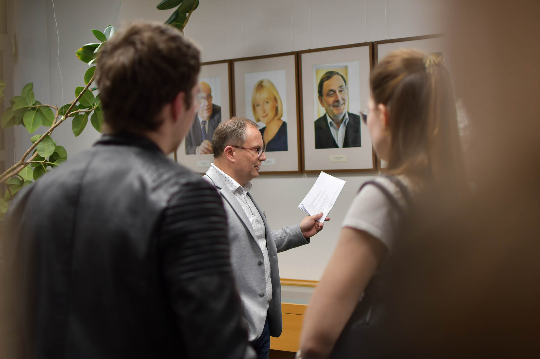 Na obrázku je pracovník Kanceláře, který lidem ukazuje fotografie bývalé ombudsmany a jejich zástupce.