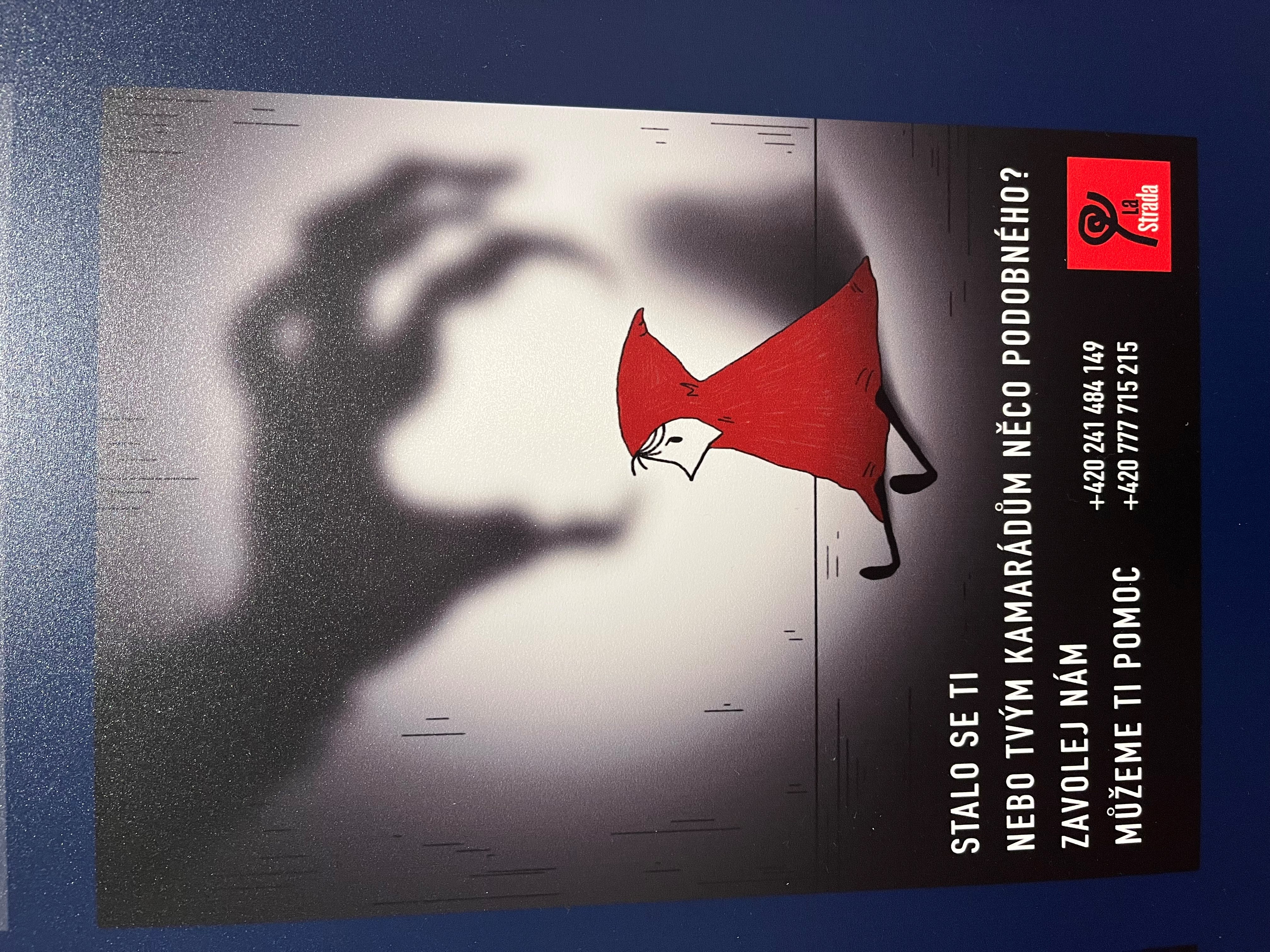 Na snímku je jeden z plakátů výstavy. Je na něm drobná postavička v rohu, po které se sápe stín ruky. Pod obrázkem jsou údaje, kam se můžou oběti vykořisťování obrátit.