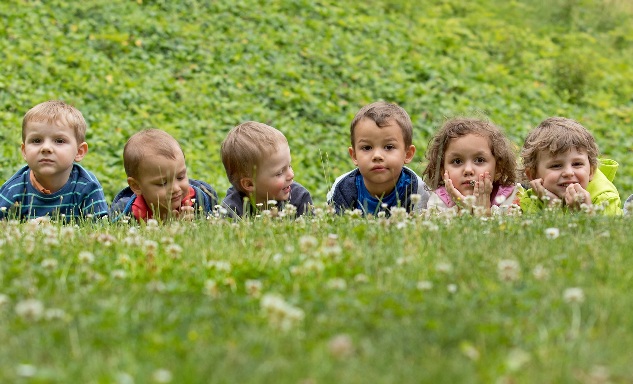 Na fotografii je šest malých dětí, které leží v trávě.