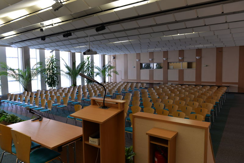 Fotografie zobrazuje velký sál, v popředí je umístěn také řečnický pult a stůl.